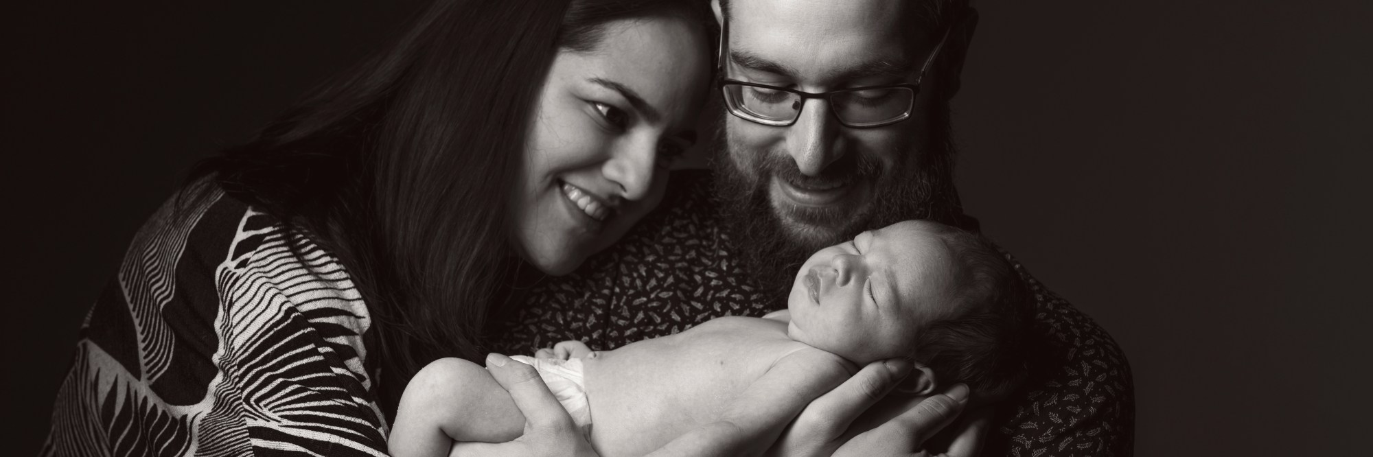 Nicole, Rob and little one posed together in a greyscale photo with black background