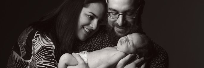 Nicole, Rob and little one posed together in a greyscale photo with black background